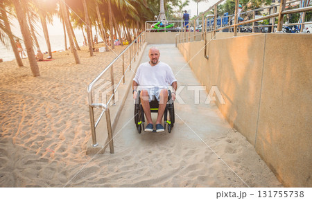Disabled man in a wheelchair moves on a ramp to the beach. 131755738