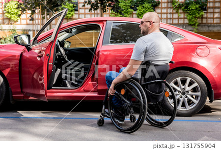 Young handicapped driver getting in red car fom wheelchair 131755904