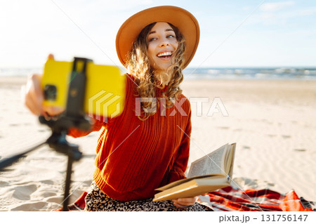Young woman sits on the beach and records a video for her subscribers. Blogging, technology concept Young woman sits on the beach and records a video for her subscribers. Blogging, technology concept 131756147
