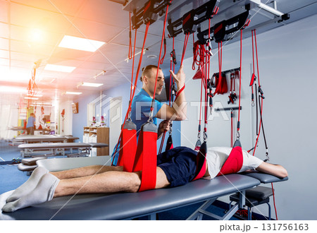 Physiotherapy. Suspension training therapy. Young man doing fitness traction Physiotherapy. Suspension training therapy. Young man doing fitness traction 131756163