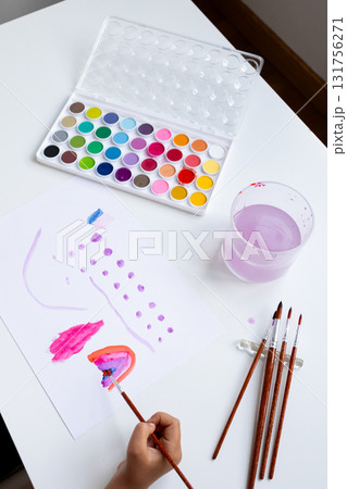 Child painting with watercolors on paper. Art supplies and creativity at play Child painting with watercolors on paper. Art supplies and creativity at play 131756271