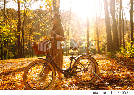 Stylish woman with a bicycle enjoying autumn weather in the park. Beautiful Woman in the autumn forest. Stylish woman with a bicycle enjoying autumn weather in the park. Beautiful Woman in the autumn forest. 131756589