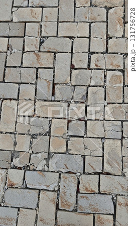 Close-up of cracked beige stone paving in a herringbone pattern on a city sidewalk. The image conveys themes of urban decay, texture and the passage of time Close-up of cracked beige stone paving in a herringbone pattern on a city sidewalk. The image conveys themes of urban decay, texture and the passage of time 131756728