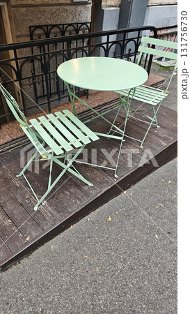 Pastel green metal chairs and table on a wooden platform outside a city building. The image suggests themes of urban leisure, simplicity and autumn solitude Pastel green metal chairs and table on a wooden platform outside a city building. The image suggests themes of urban leisure, simplicity and autumn solitude 131756730