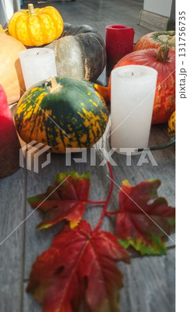 Assorted pumpkins, candles and red autumn leaves arranged on a wooden floor in warm sunlight. The image represents cozy fall ambiance, seasonal decor and festive home atmosphere Assorted pumpkins, candles and red autumn leaves arranged on a wooden floor in warm sunlight. The image represents cozy fall ambiance, seasonal decor and festive home atmosphere 131756735