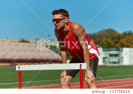 Athlete resting on hurdle after intense training session on sunny track Athlete resting on hurdle after intense training session on sunny track 131756818