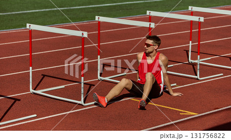 Athlete resting on track between hurdles after training under sunlight 131756822