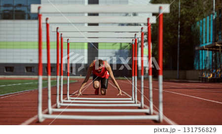 Runner preparing to start hurdle sprint on athletics track under sunlight 131756829