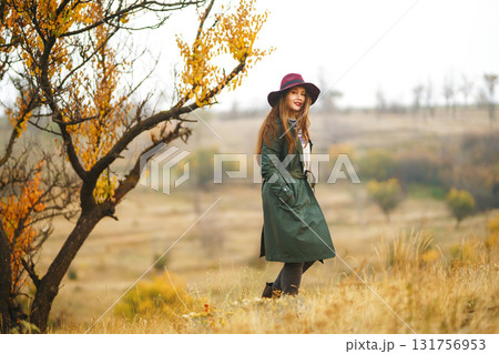 Beautiful stylish girl walks in the autumn park. The girl is dressed in a green coat and a red hat. 131756953