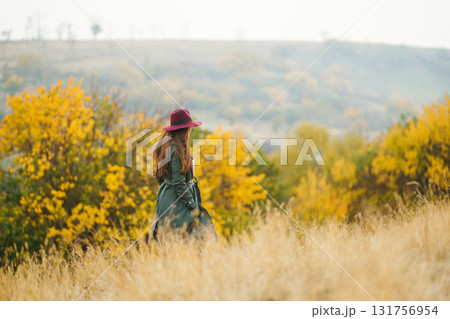 Beautiful stylish girl walks in the autumn park. The girl is dressed in a green coat and a red hat. 131756954