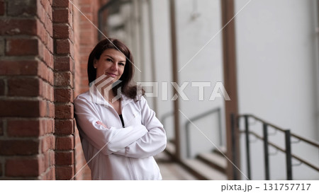 A confident woman in a white jacket leans against a brick wall, smiling gently. Her relaxed pose and urban setting reflect a modern, balanced lifestyle, emphasizing self-confidence and contentment. A confident woman in a white jacket leans against a brick wall, smiling gently. Her relaxed pose and urban setting reflect a modern, balanced lifestyle, emphasizing self-confidence and contentment. 131757717