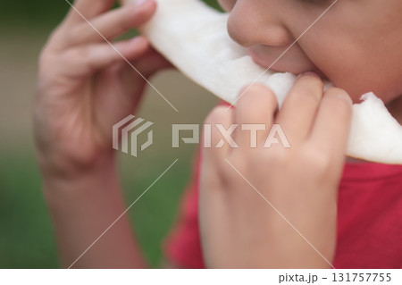 A child savors a fresh melon slice, his attention captured in the act. This image invites viewers to appreciate the freshness of summer produce. A child savors a fresh melon slice, his attention captured in the act. This image invites viewers to appreciate the freshness of summer produce. 131757755