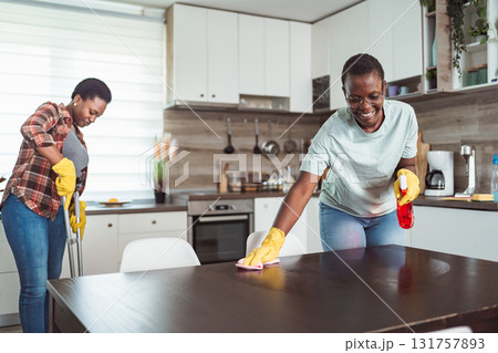 Two cheerful black women cleaning the kitchen table and floor Two cheerful black women cleaning the kitchen table and floor 131757893
