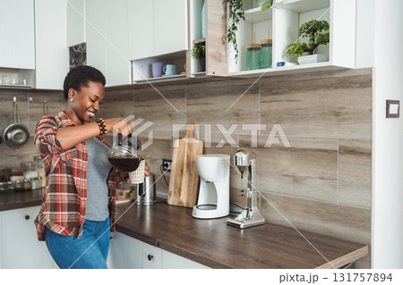 Young woman pouring coffee in a mug in her kitchen 131757894
