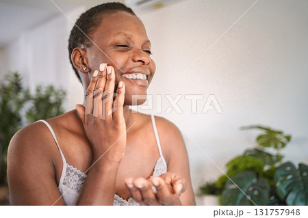 Happy young woman applying face cream smiling at home 131757948