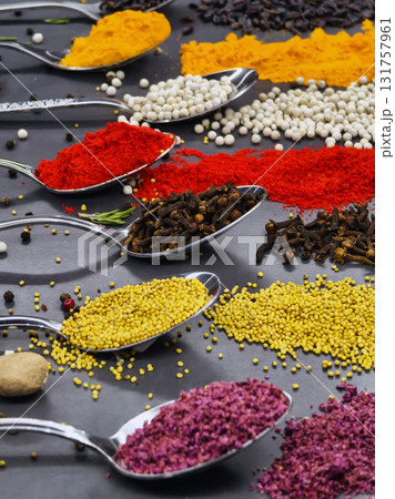 Colorful spices arranged in spoons on a black surface showcasing culinary variety and texture 131757961
