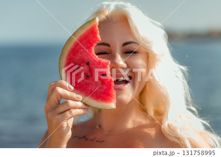Watermelon Woman Summer Beach: Happy blonde playfully holds watermelon slice near face, outdoors, sunny day. 131758995
