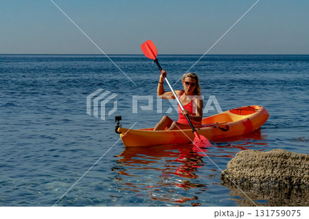 Woman, kayak, paddling a bright orange boat in the clear blue sea, enjoying summer vacation Woman, kayak, paddling a bright orange boat in the clear blue sea, enjoying summer vacation 131759075