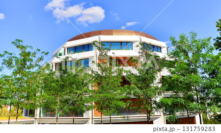 A residential building by lush green trees and surrounded by fresh vegetation on a clear sunny day. Modern architecture residential apartment building complex surrounded by greenery. A residential building by lush green trees and surrounded by fresh vegetation on a clear sunny day. Modern architecture residential apartment building complex surrounded by greenery. 131759283