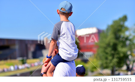 The boy is sitting on dad's shoulders, they are looking at buildings. The boy is sitting on dad's shoulders, they are looking at buildings. 131759555