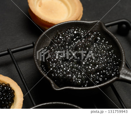 Black caviar in cast iron pans and tartlet on dark board.  Top view 131759943