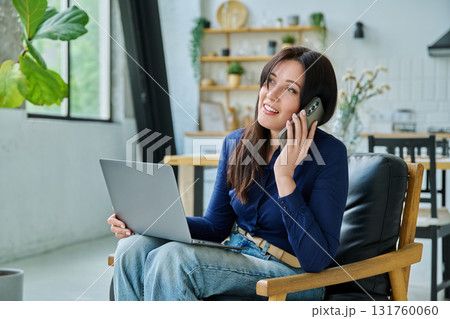 Positive young woman working at home with laptop talking on phone 131760060