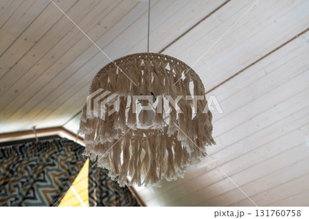 Macrame lamp, wooden ceiling, bohemian decor, stylish pendant light fixture hangs from white slatted planks creating a cozy home atmosphere 131760758