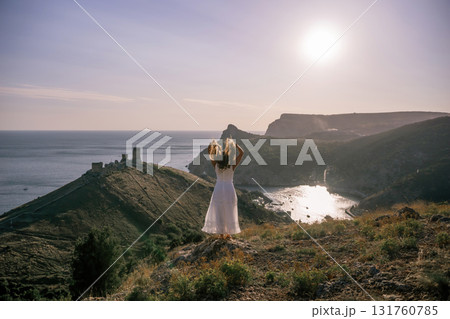 woman stands on a hill overlooking the ocean, her arms raised in the air. Concept of freedom and joy, as if the woman is celebrating a moment of happiness or accomplishment. woman stands on a hill overlooking the ocean, her arms raised in the air. Concept of freedom and joy, as if the woman is celebrating a moment of happiness or accomplishment. 131760785