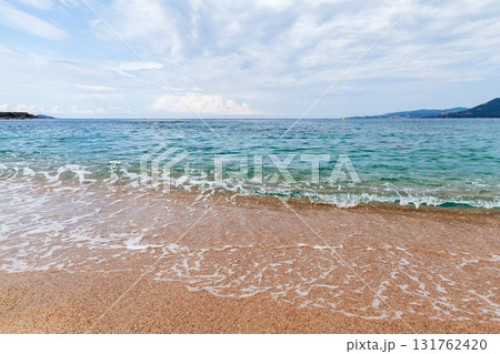 Shore water covers sandy beach of Propriano under cloudy blue sky Shore water covers sandy beach of Propriano under cloudy blue sky 131762420
