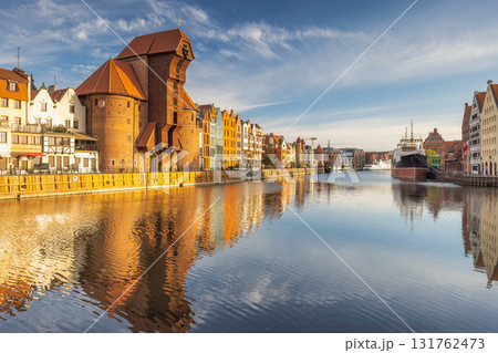Gdansk with medieval port crane over The Motlawa river, a city on the Baltic coast of northern Poland, Europe. Scenic cityscape with historic buildings reflecting in calm river under a blue sky. 131762473