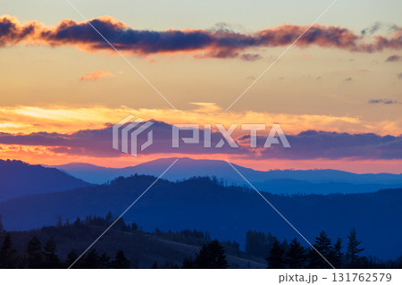 A vibrant sunrise sky with pastel orange hues and purplish clouds over a hazy blue mountain range. A vibrant sunrise sky with pastel orange hues and purplish clouds over a hazy blue mountain range. 131762579
