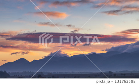 Mountain silhouettes under a painted sky, sunrise's soft hues ignite the horizon. Nature's spectacle unfolds. 131762588