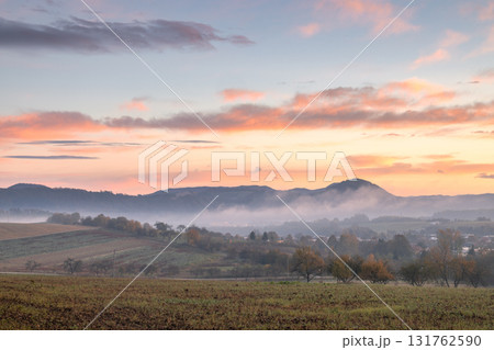 Serene landscape with rolling hills shrouded in mist, painted by a vibrant sunrise sky. Beautiful light 131762590