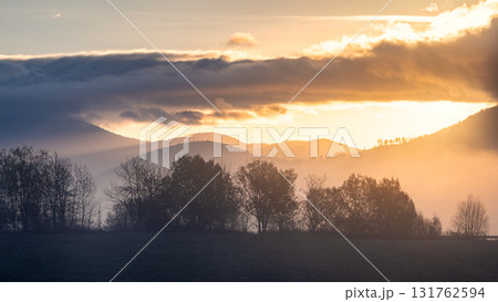 Golden light graces rolling hills with atmospheric clouds, serene vista, and nature's beauty. 131762594