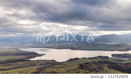 The Liptovska Mara dam in northern Slovakia, Europe. Dramatic mountain landscape featuring a serene lake and expansive cloudy skies. Rolling hills in foreground. The Liptovska Mara dam in northern Slovakia, Europe. Dramatic mountain landscape featuring a serene lake and expansive cloudy skies. Rolling hills in foreground. 131762609