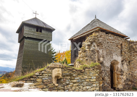 Wooden church in The Liptovska Anna village in northern Slovakia, Europe. Historic wooden church tower and stone structure ruins against cloudy skies and fall colors landscape. 131762623