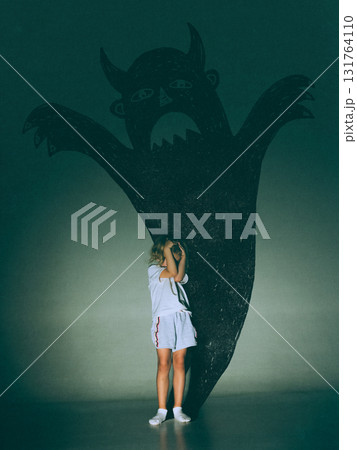 Creative digital artwork. Little girl covering eyes before giant devil shadow on green wall 131764110