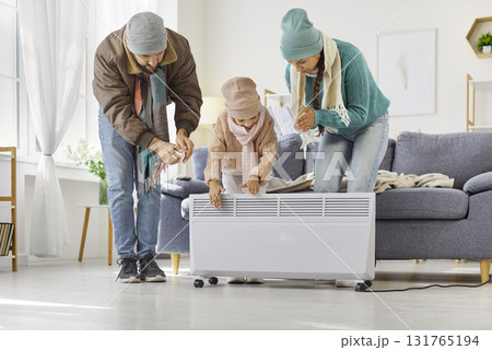 Family adjusting portable electric heater at home to stay warm during winter Family adjusting portable electric heater at home to stay warm during winter 131765194