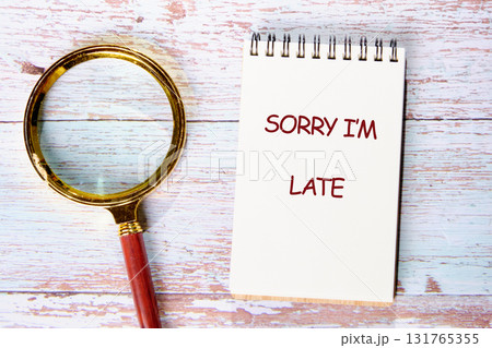 On a wooden surface, a notepad displays SORRY I AM LATE next to a magnifying glass, suggesting humorous exploration of tardiness and time management On a wooden surface, a notepad displays SORRY I AM LATE next to a magnifying glass, suggesting humorous exploration of tardiness and time management 131765355