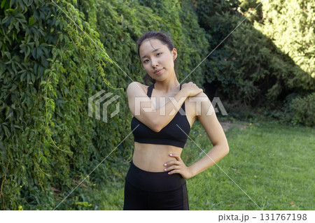 The woman is standing outdoors and posing with her hand on her shoulder The woman is standing outdoors and posing with her hand on her shoulder 131767198