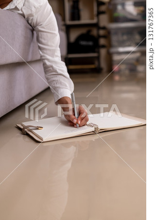 A person is writing on a notepad placed on the floor 131767365