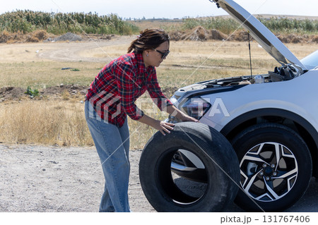Woman changing tire on a car in a parking lot Woman changing tire on a car in a parking lot 131767406