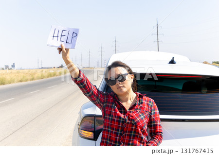 woman is standing on the side of a road next to her car,holding up a sign HELP woman is standing on the side of a road next to her car,holding up a sign HELP 131767415