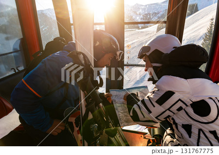 Scenic two skiers study trail map inside ski lift gondola at warm sunrise light at mountain alpine resort. Scenery group friends teamwork, planning, and excitement downhill winter sports adventure 131767775