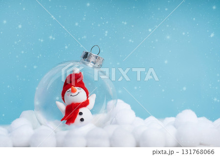 Cute snowman inside a glass ornament among artificial snowdrifts on a blue bokeh background. Christmas background with copy space for greeting cards, banners and holiday promos. Cute snowman inside a glass ornament among artificial snowdrifts on a blue bokeh background. Christmas background with copy space for greeting cards, banners and holiday promos. 131768066