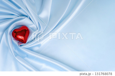 Elegant blue satin drape with red glass heart ornament. Romantic background for Valentine, wedding or Christmas gift themes. Elegant blue satin drape with red glass heart ornament. Romantic background for Valentine, wedding or Christmas gift themes. 131768078