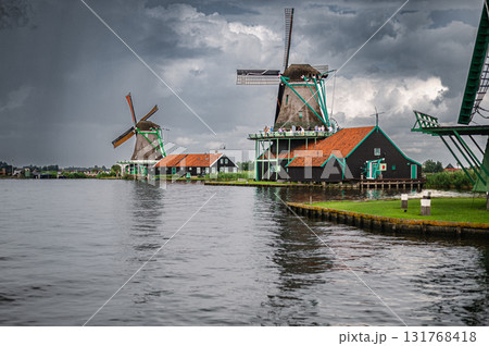 Scenic view of traditional Dutch windmills in Zaandam with changing skies, from calm daylight to approaching rain. 131768418