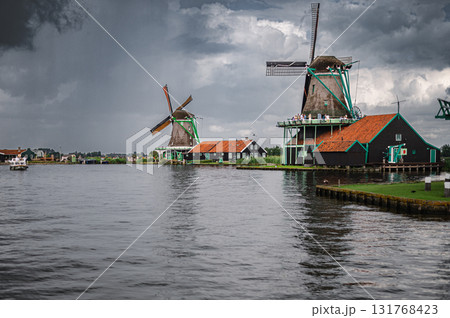 Scenic view of traditional Dutch windmills in Zaandam with changing skies, from calm daylight to approaching rain. 131768423