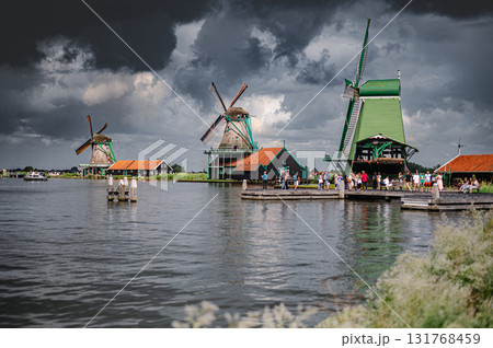 Scenic view of traditional Dutch windmills in Zaandam with changing skies, from calm daylight to approaching rain. Scenic view of traditional Dutch windmills in Zaandam with changing skies, from calm daylight to approaching rain. 131768459