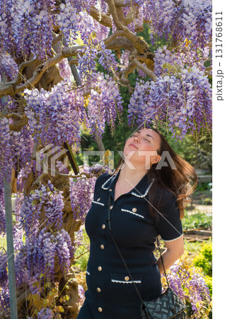 Young beautiful woman standing gracefully beside cascading purple wisteria flowers in bloom. 131768611